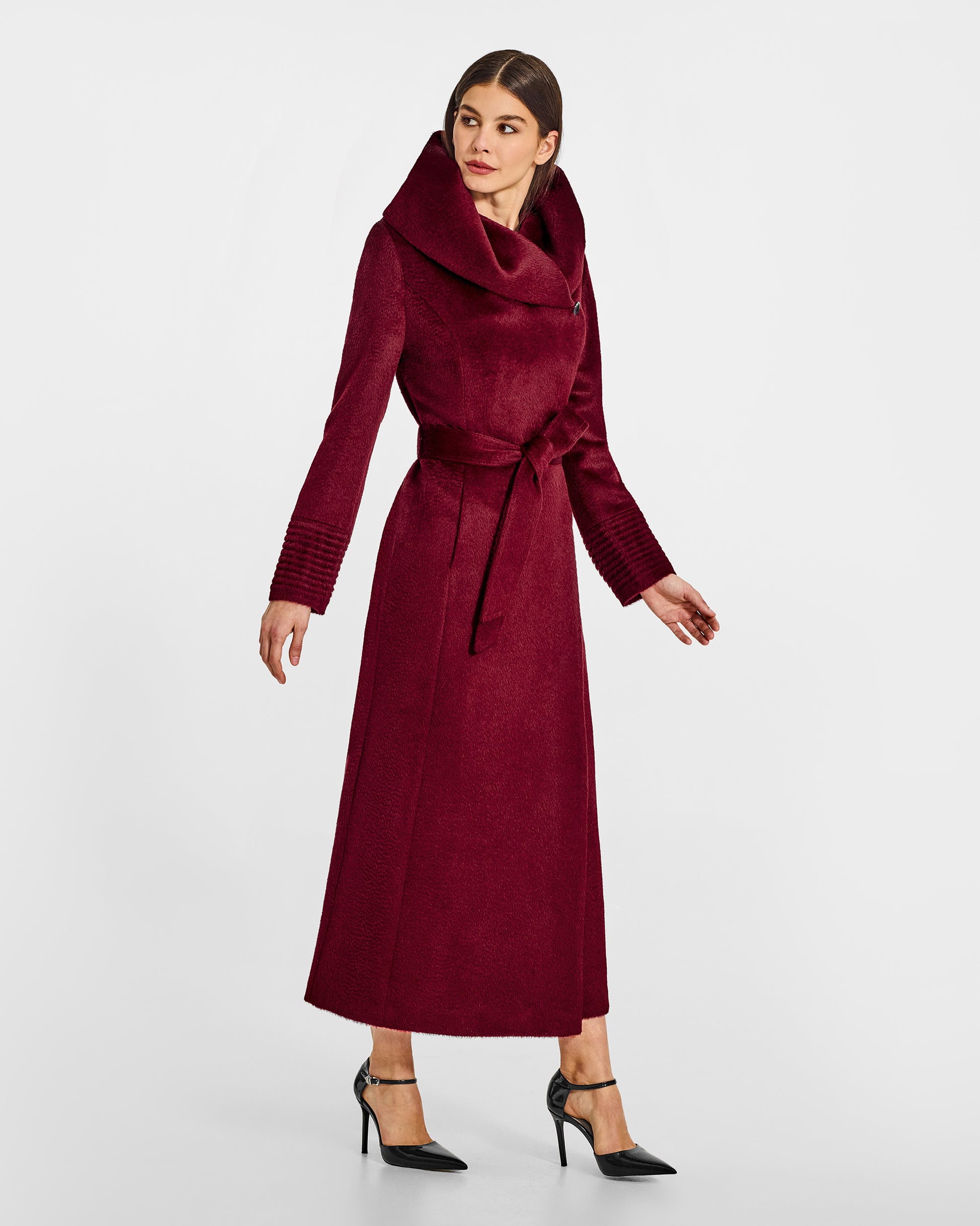 Side view of model wearing a Sentaler maxi bordeaux coat made of suri alpaca wool, with a hooded collar, worn belted.