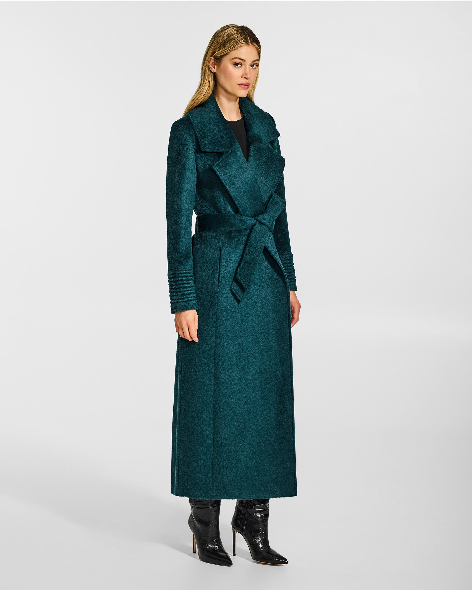Side view of model wearing a Sentaler emerald green maxi coat made of suri alpaca wool, with a notched collar, worn belted.