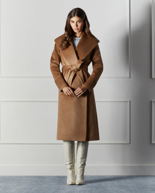 Front view of model wearing a Sentaler long dark camel wrap coat made of suri alpaca wool, with a shawl collar, worn belted.