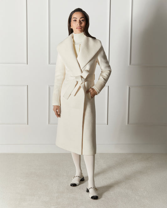 Front view of model wearing a Sentaler long ivory wrap coat made of suri alpaca wool, with a shawl collar, worn belted.