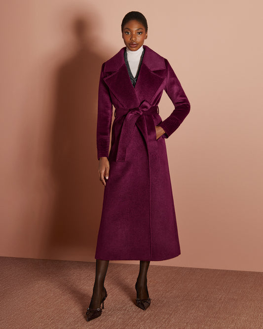 Front view of model wearing a Sentaler cherry lacquer maxi coat made of suri alpaca wool, with a notched collar, worn belted.