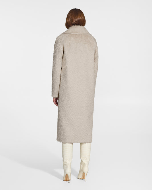 Back view of model wearing a Sentaler oat notched collar coat made of textured suri alpaca wool, with raglan sleeves, worn buttoned.