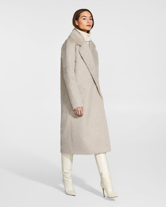 Side view of model wearing a Sentaler oat notched collar coat made of textured suri alpaca wool, with raglan sleeves, worn buttoned.