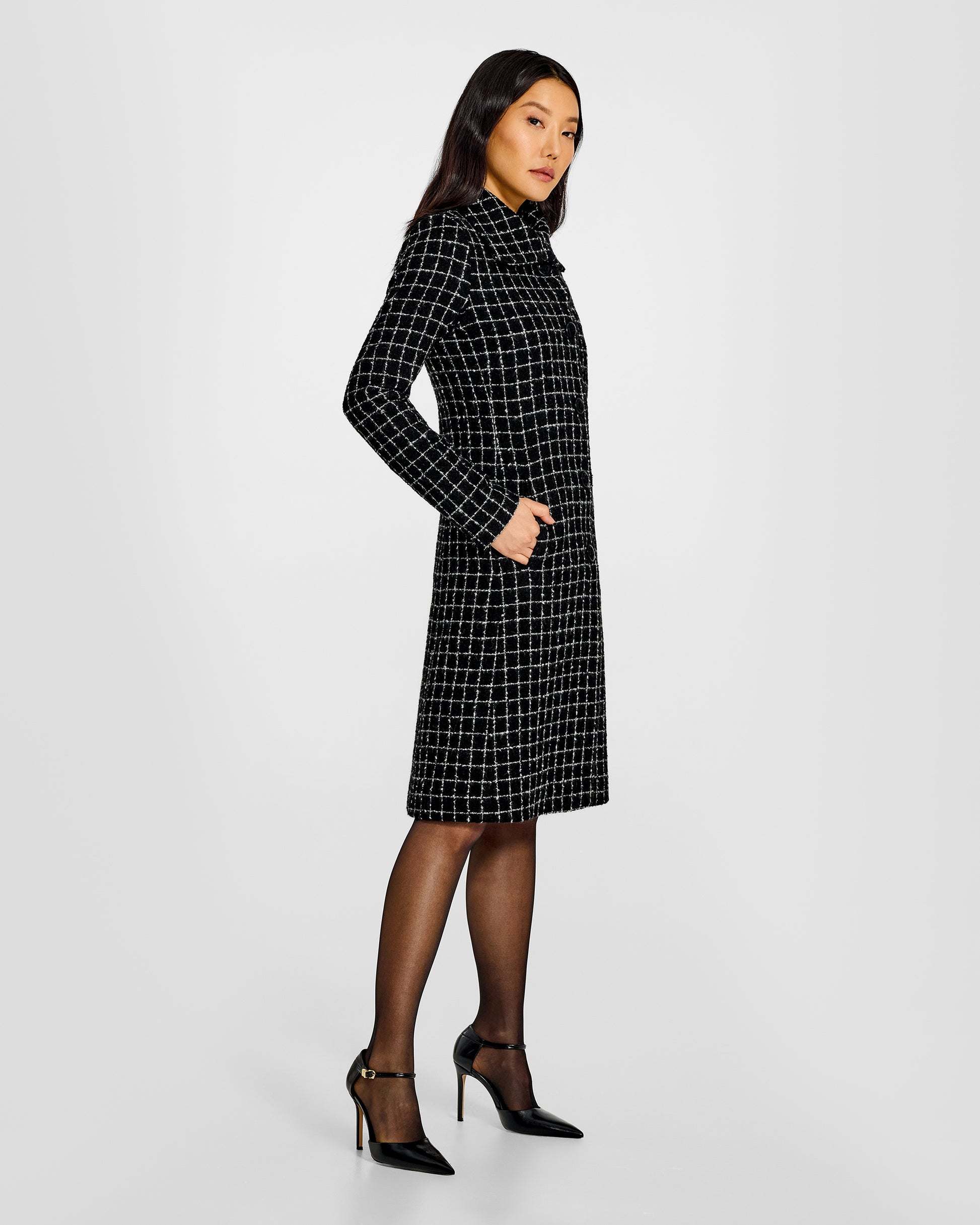 Side view of model wearing a Sentaler black check A-line coat made of tweed suri alpaca wool, worn buttoned.
