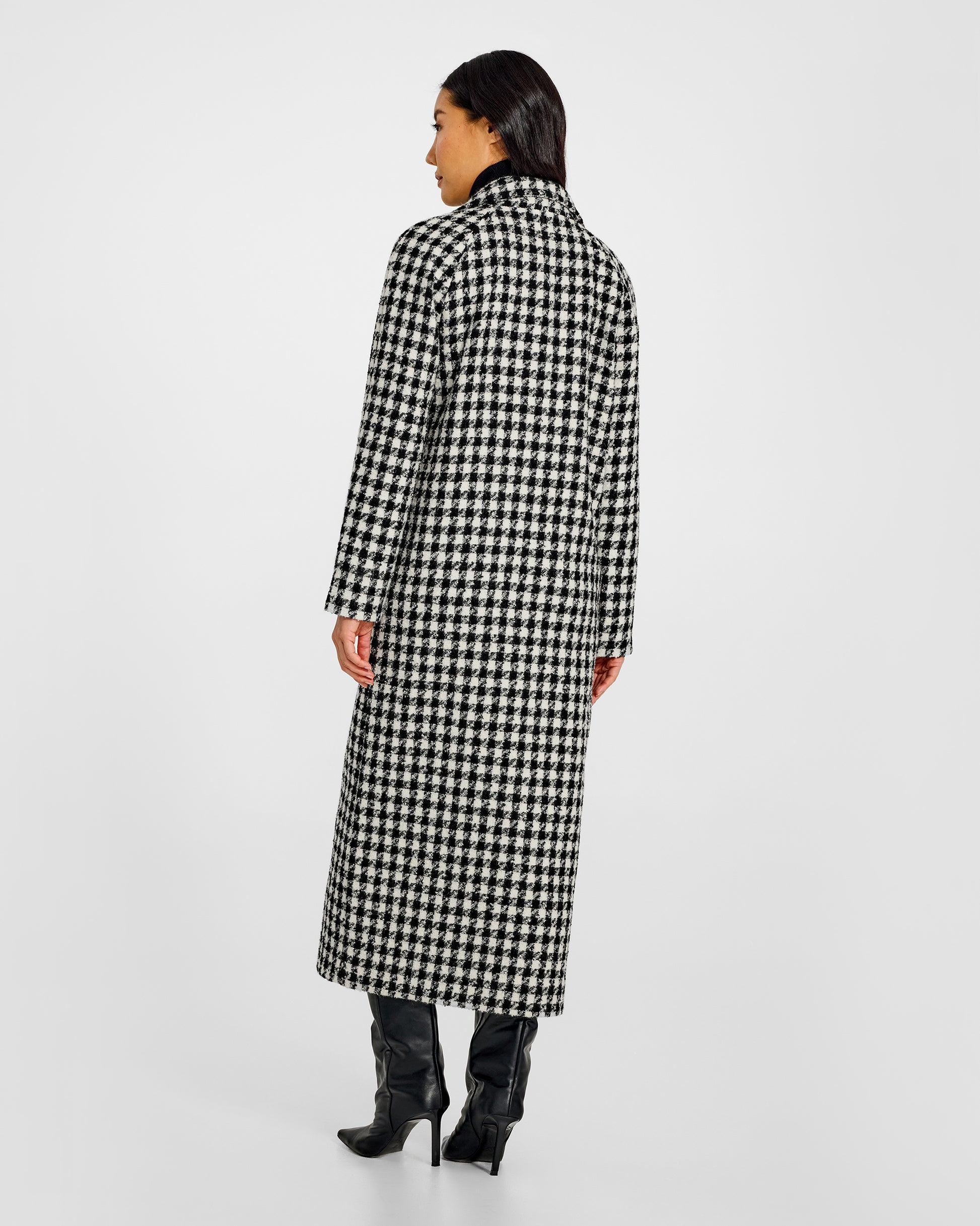 Bacl view of model wearing a Sentaler black and white houndstooth long coat made of tweed suri alpaca wool, worn buttoned.