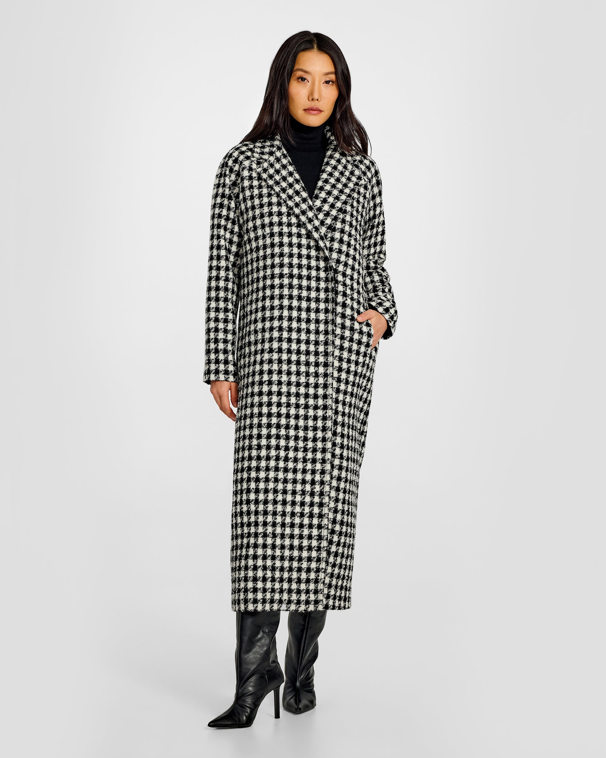 Front view of model wearing a Sentaler black and white houndstooth long coat made of tweed suri alpaca wool, worn buttoned.