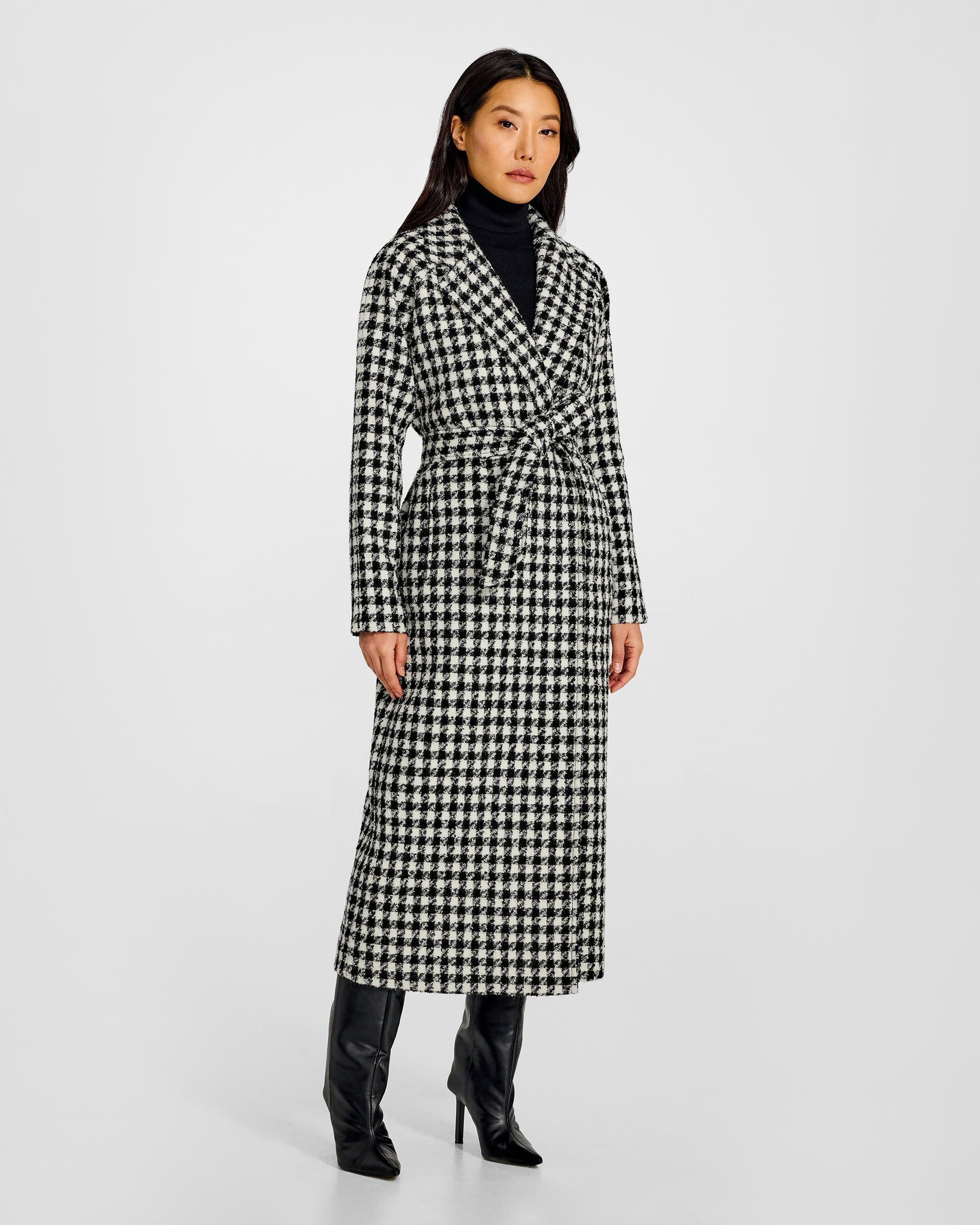Front view of model wearing a Sentaler black and white houndstooth long coat made of tweed suri alpaca wool, worn belted.