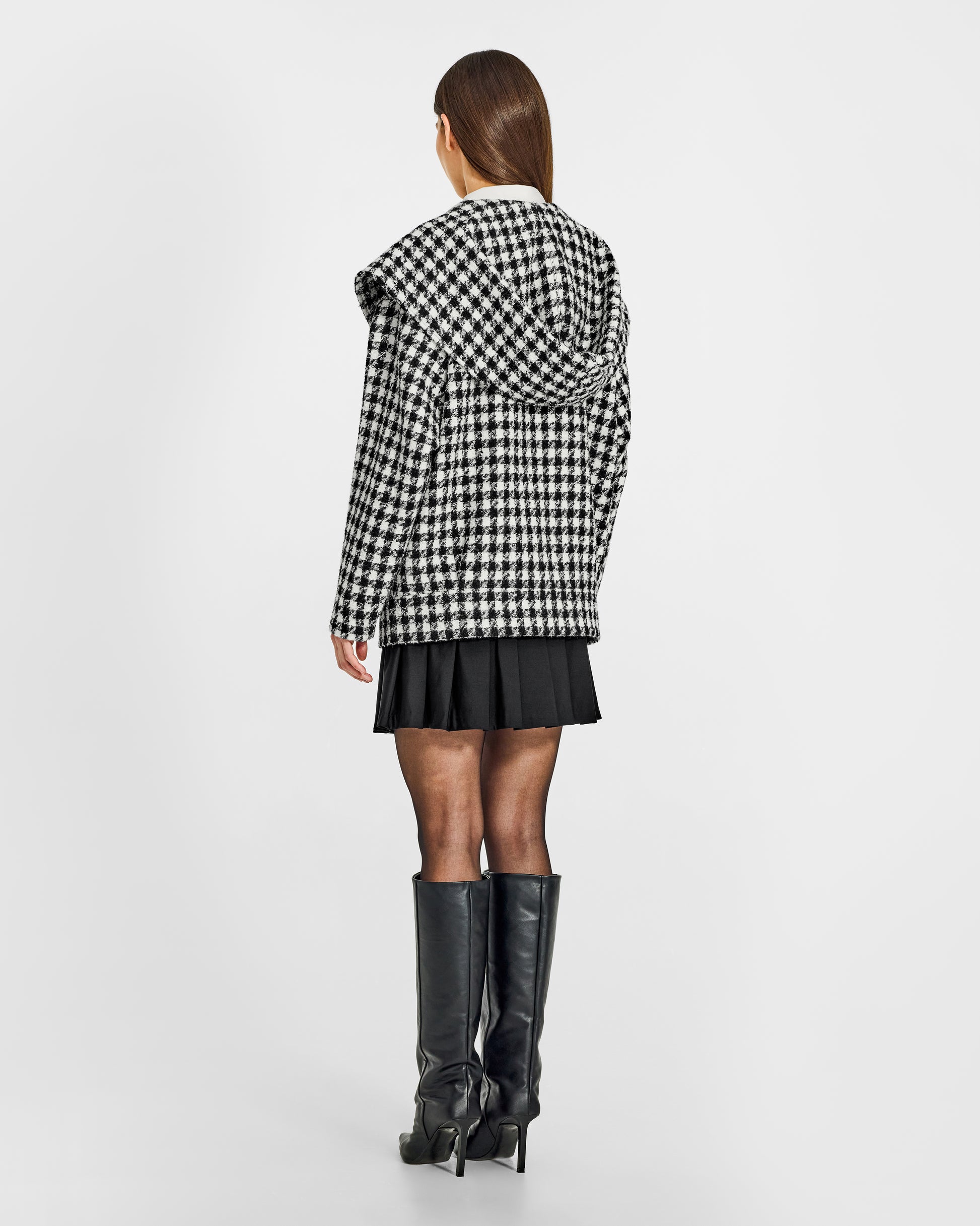 Back view of model wearing a Sentaler black and white houndstooth jacket made of tweed suri alpaca wool, with hood, worn buttoned.