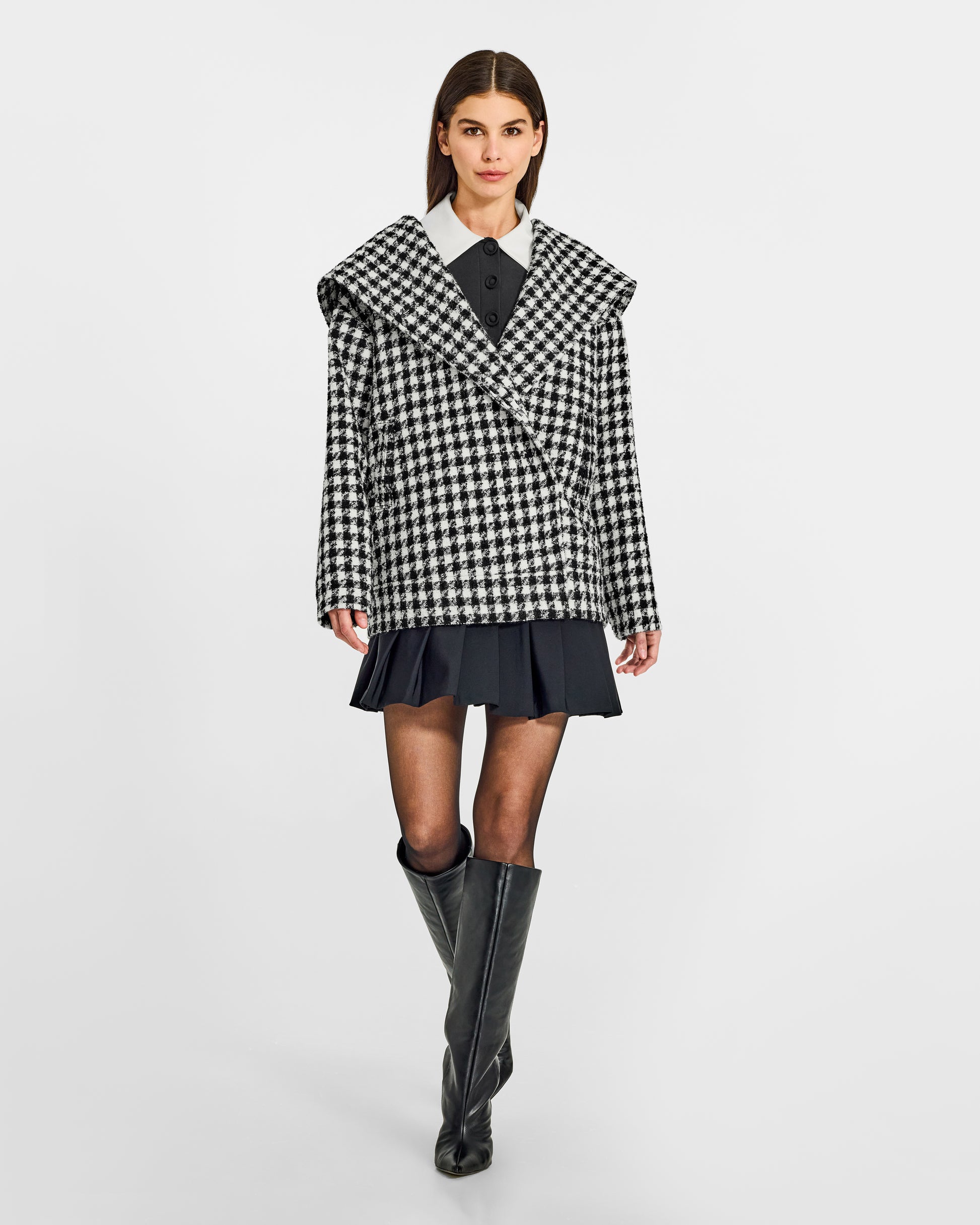 Front view of model wearing a Sentaler black and white houndstooth jacket made of tweed suri alpaca wool, with hood, worn buttoned.