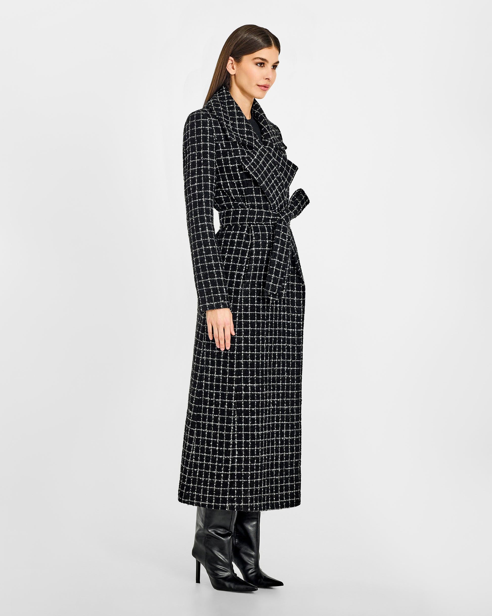 Side view of model wearing a Sentaler black check maxi coat made of tweed suri alpaca wool, with a notched collar, worn belted.