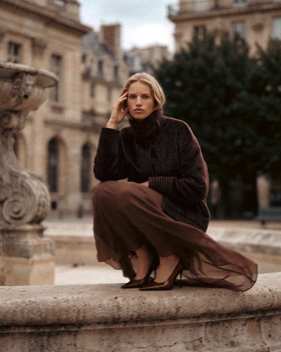 SENTALER Suri Alpaca Stand Collar Aviator Jacket in Chocolate Brown, worn seated on a stone fountain surround in Paris.