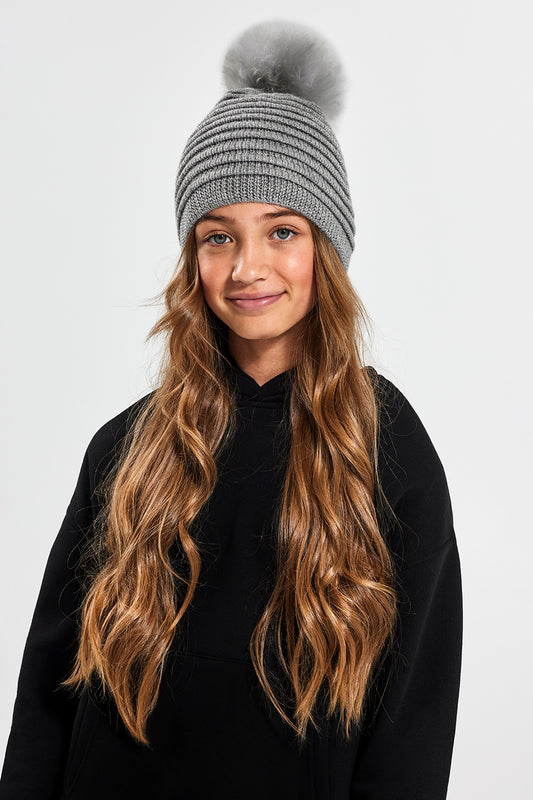 Sentaler Kids (6-14 Years) Ribbed Hat with Oversized Fur Pompon featured in Baby Alpaca and available in Grey. Seen from front on model above the waist.